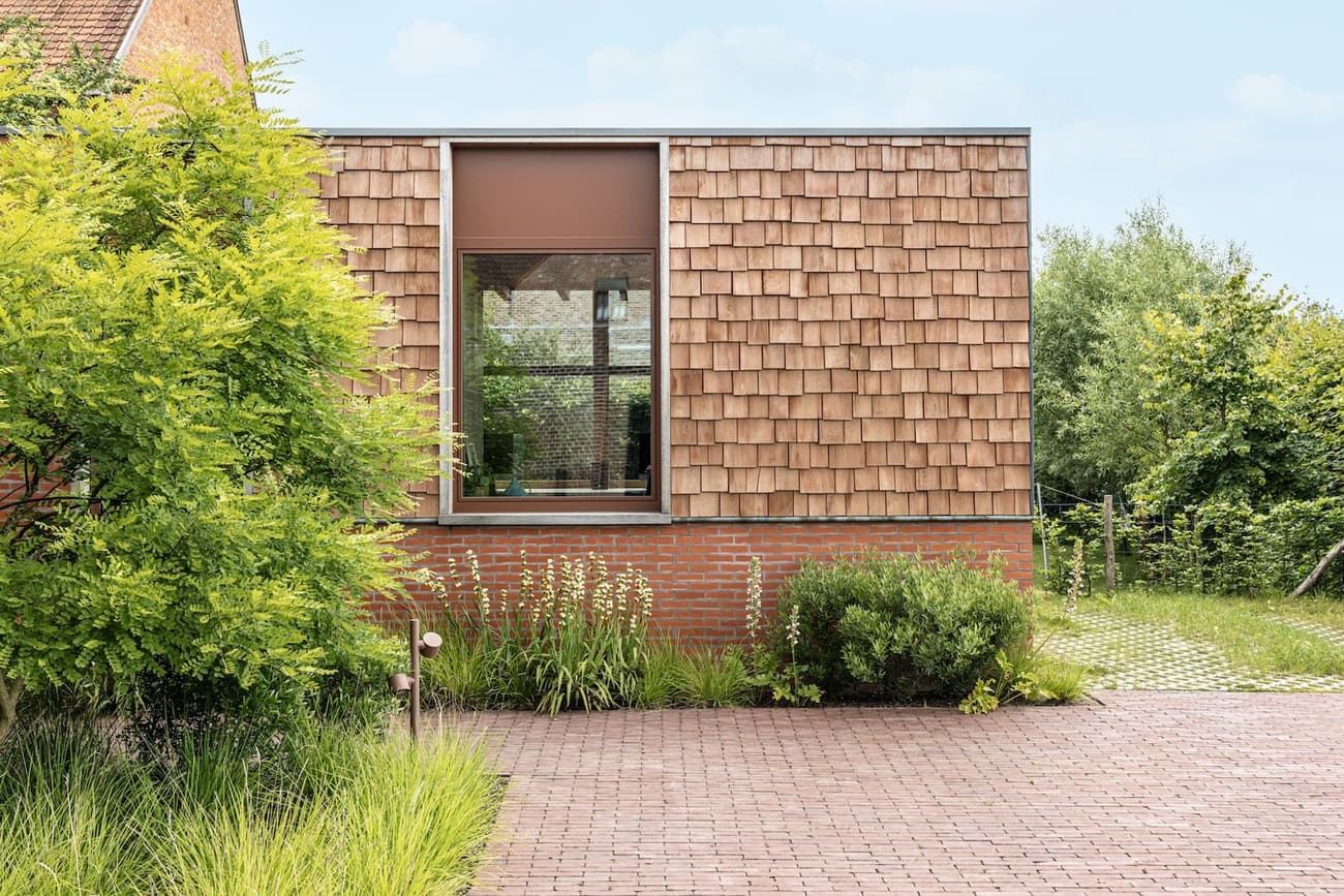 Architectural project - brick wall, garden integration, landscaping, home exterior, built environment, natural materials, wood, timber, outdoor space, outdoor living, sustainable design, warm tones, eco design, green building, green, neutral tones, beige, brown, exterior wall, daylight optimization, rustic modern, exterior, tranquil setting, natural landscape, modern rustic, biophilic design, passive house, natural ventilation, modern facade, timber cladding, eco friendly home, countryside home, large window, wooden shingles, brick, landscape design, red brick, garden view, nature integration, earthy palette, inviting exterior, textured facade, contemporary facade, garden path, green surroundings, simple architecture, residential facade, red