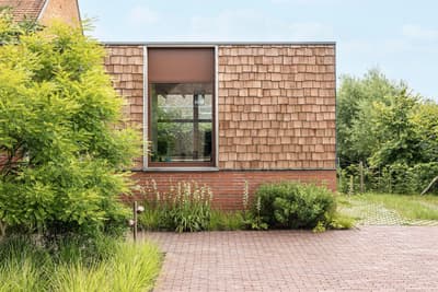 Architectural project - brick wall, garden integration, landscaping, home exterior, built environment, natural materials, wood, timber, outdoor space, outdoor living, sustainable design, warm tones, eco design, green building, green, neutral tones, beige, brown, exterior wall, daylight optimization, rustic modern, exterior, tranquil setting, natural landscape, modern rustic, biophilic design, passive house, natural ventilation, modern facade, timber cladding, eco friendly home, countryside home, large window, wooden shingles, brick, landscape design, red brick, garden view, nature integration, earthy palette, inviting exterior, textured facade, contemporary facade, garden path, green surroundings, simple architecture, residential facade, red