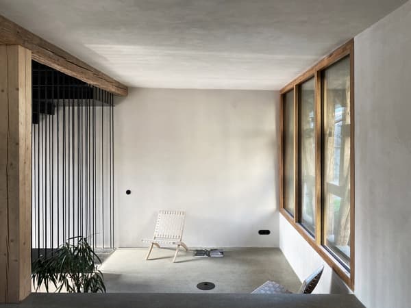 Architectural project - floor to ceiling windows, raw elegance, woven chair, muted colors, potted plant, minimalist room, airy vibe, quiet space, filtered light, relaxing nook, reading chair, serene room, inviting vibe, open feeling, natural materials, natural light, sustainable design, light wood, eco friendly, Scandinavian influence, simple design, natural textures, cozy retreat, neutral palette, tranquil setting, contemporary home, modern minimalism, clean lines, white walls, light filled, large windows, architectural simplicity, wood frame, timber accents, beige tones, airy space, plaster finish, cozy corner, modern home, calm atmosphere, interior space, peaceful atmosphere, Japandi style, indoor plants, residential interior