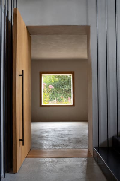 Architectural project - open doorway, polished concrete, entrance hall, spacious feeling, transition space, pared-back style, airy ambiance, seamless connection, elemental design, eco-friendly design, wood, timber, raw materials, wooden frame, natural light, grey, neutral tones, daylight, beige, concrete, light wood, low carbon design, Scandinavian influence, natural textures, minimalist vibe, serene space, sustainable building, earth tones, sustainable home, passive house, clean lines, indoor outdoor, architectural simplicity, Nordic style, open plan, organic materials, garden view, bright interior, modern home, sleek design, simple decor, concrete floor, biophilic elements, smooth surfaces, energy efficiency, hallway, understated elegance, tranquility, minimalist interior, timber door, wood door