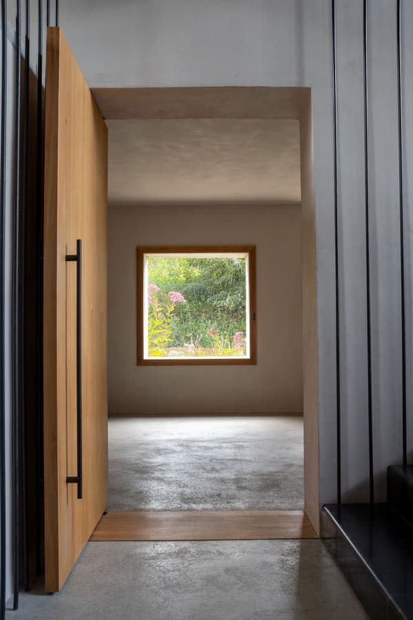 Architectural project - open doorway, polished concrete, entrance hall, spacious feeling, transition space, pared-back style, airy ambiance, seamless connection, elemental design, eco-friendly design, wood, timber, raw materials, wooden frame, natural light, grey, neutral tones, daylight, beige, concrete, light wood, low carbon design, Scandinavian influence, natural textures, minimalist vibe, serene space, sustainable building, earth tones, sustainable home, passive house, clean lines, indoor outdoor, architectural simplicity, Nordic style, open plan, organic materials, garden view, bright interior, modern home, sleek design, simple decor, concrete floor, biophilic elements, smooth surfaces, energy efficiency, hallway, understated elegance, tranquility, minimalist interior, timber door, wood door
